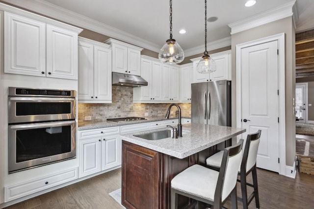 kitchen with white cabinetry, sink, light stone counters, stainless steel appliances, and a center island with sink