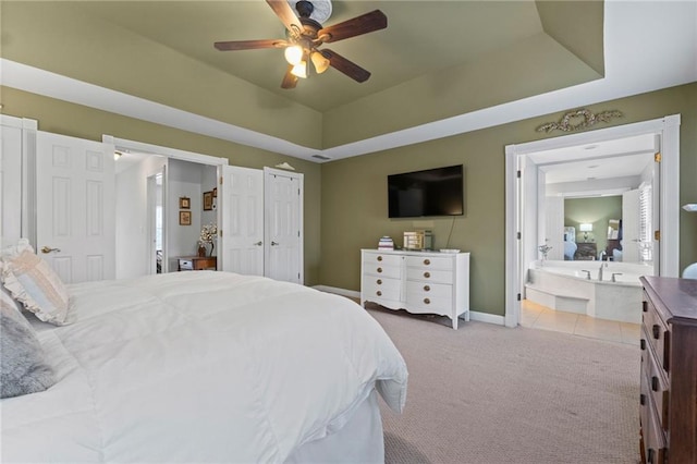 bedroom featuring ceiling fan, light colored carpet, ensuite bathroom, and a tray ceiling