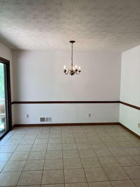 tiled empty room with an inviting chandelier and a textured ceiling