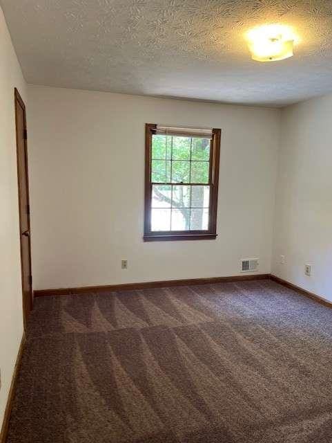 empty room with dark carpet and a textured ceiling