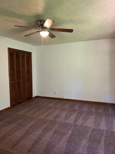 unfurnished bedroom with ceiling fan, dark carpet, a closet, and a textured ceiling