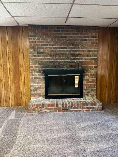 room details with wooden walls, a fireplace, carpet flooring, and a paneled ceiling