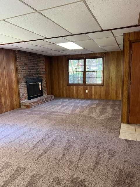 unfurnished living room with a brick fireplace, carpet floors, and wooden walls