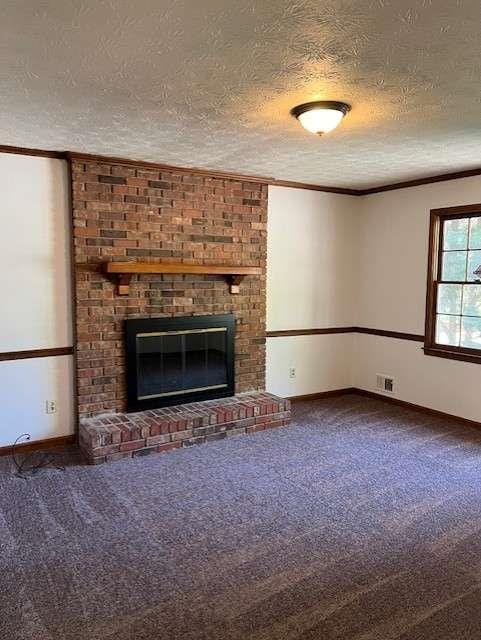 unfurnished living room with crown molding, a fireplace, carpet, and a textured ceiling