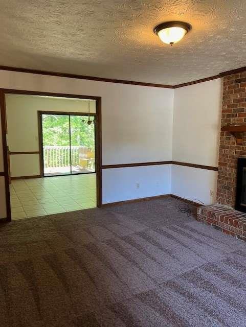 unfurnished living room with light carpet, a brick fireplace, ornamental molding, and a textured ceiling