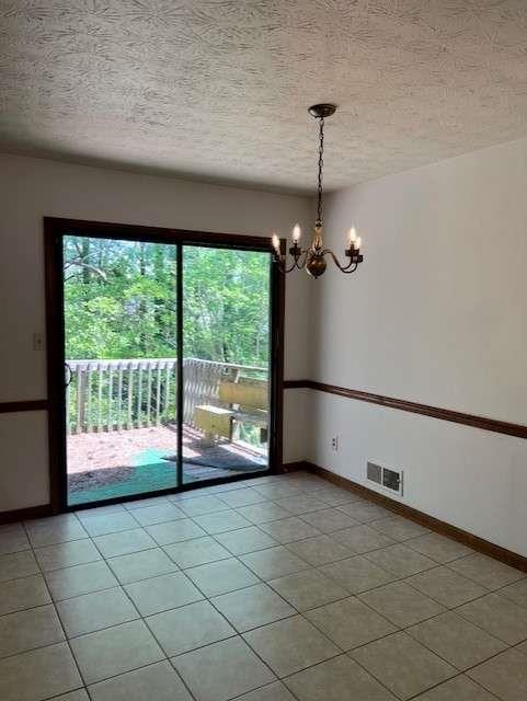 tiled empty room with a notable chandelier and a textured ceiling