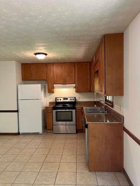 kitchen featuring light tile patterned flooring, sink, stainless steel range with electric stovetop, white fridge, and a textured ceiling