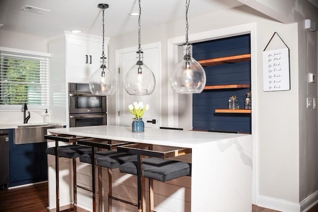 kitchen featuring a kitchen bar, sink, light stone counters, multiple ovens, and decorative light fixtures