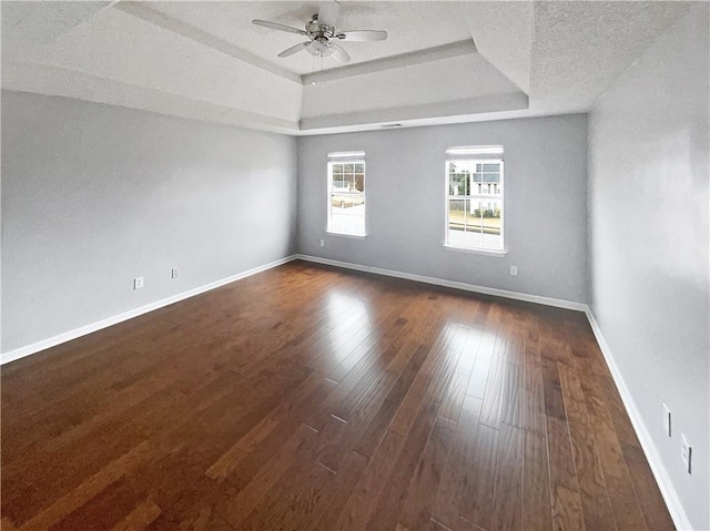 spare room featuring a tray ceiling, ceiling fan, dark hardwood / wood-style flooring, and a textured ceiling