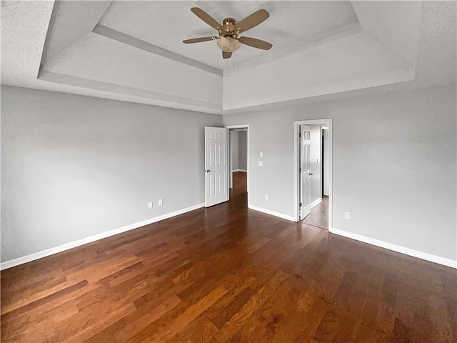 spare room with a tray ceiling, ceiling fan, and dark wood-type flooring