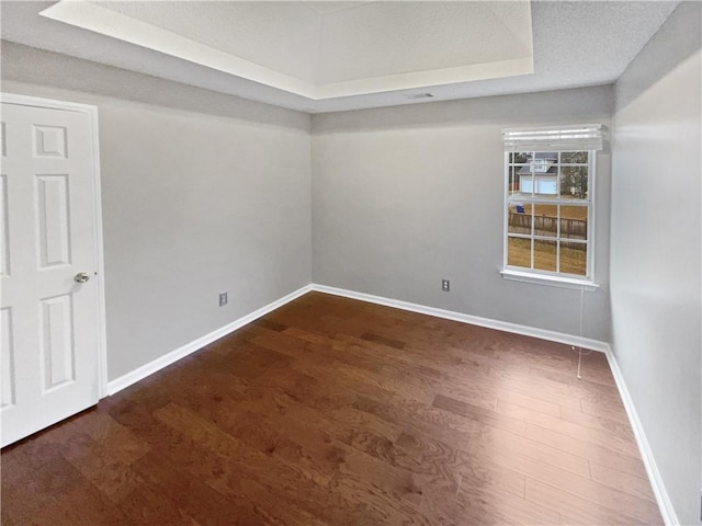 spare room featuring a raised ceiling, dark wood-type flooring, and a textured ceiling