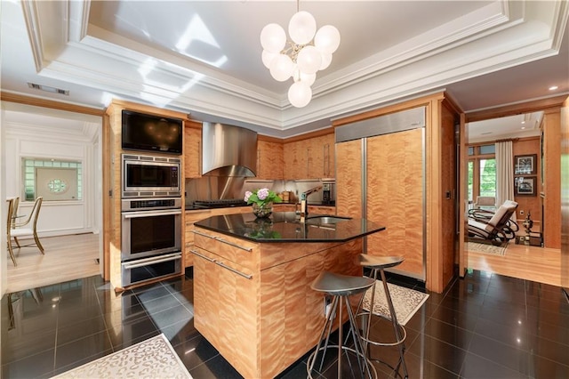 kitchen featuring sink, wall chimney exhaust hood, a notable chandelier, built in appliances, and an island with sink