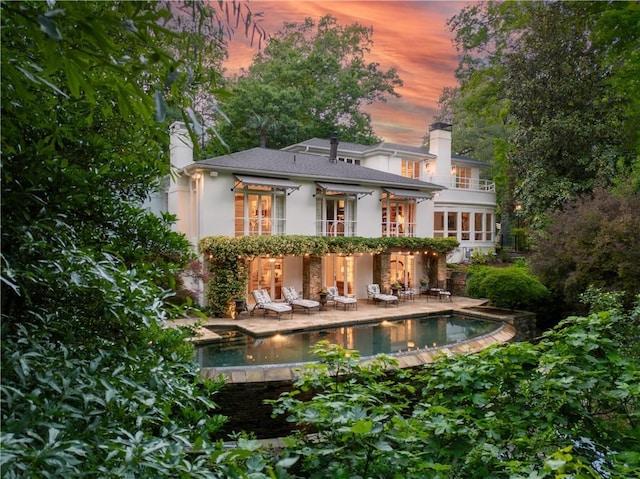 back house at dusk featuring a balcony and a patio area