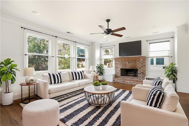 living room featuring a brick fireplace, dark hardwood / wood-style floors, crown molding, and ceiling fan