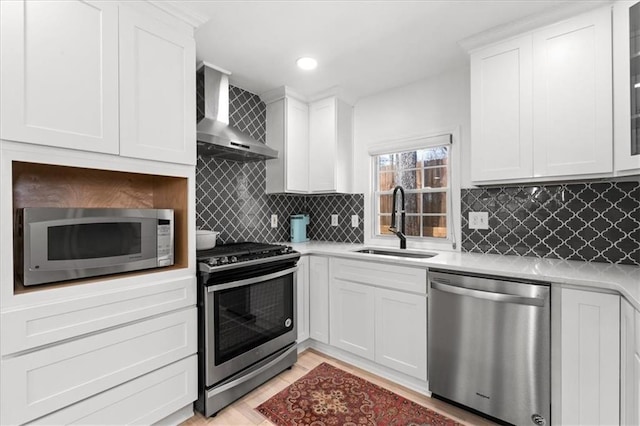 kitchen with light countertops, wall chimney range hood, appliances with stainless steel finishes, and a sink