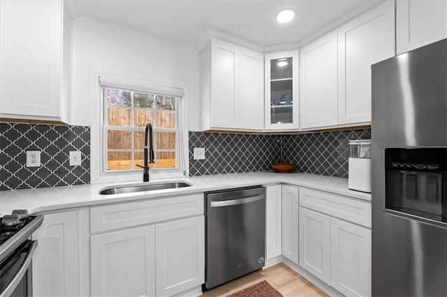 kitchen with a sink, light countertops, glass insert cabinets, appliances with stainless steel finishes, and white cabinetry