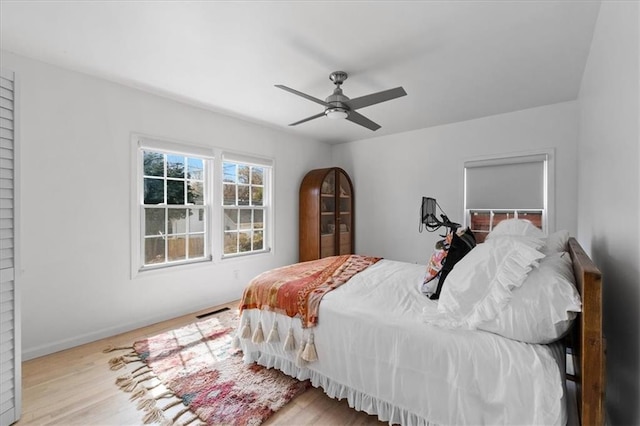 bedroom with ceiling fan, wood finished floors, visible vents, and baseboards