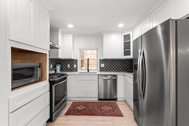 kitchen featuring under cabinet range hood, appliances with stainless steel finishes, light countertops, and a sink