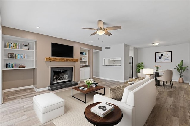 living room with built in shelves, light wood-type flooring, and ceiling fan