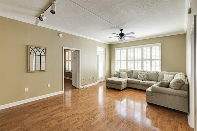 living area with a textured ceiling, wood finished floors, rail lighting, crown molding, and baseboards