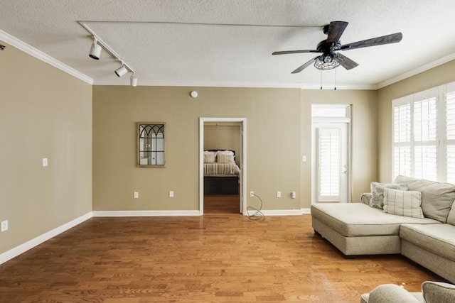 living room with crown molding, ceiling fan, baseboards, light wood-type flooring, and a textured ceiling