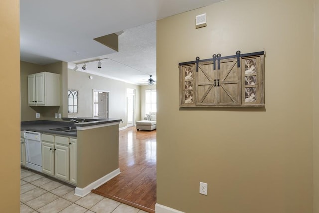 kitchen featuring a ceiling fan, white dishwasher, a sink, rail lighting, and dark countertops