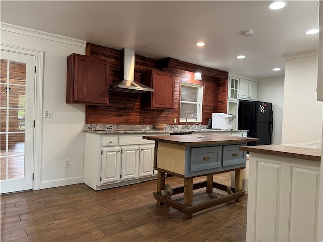 kitchen with black refrigerator, wooden counters, white cabinets, and wall chimney range hood