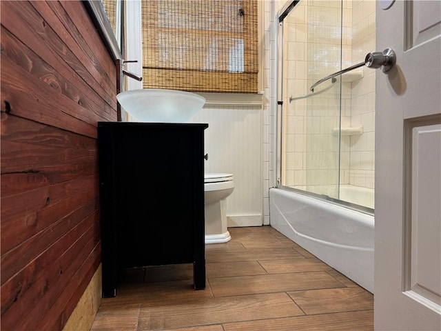 full bathroom with vanity, wooden walls, hardwood / wood-style floors, enclosed tub / shower combo, and toilet