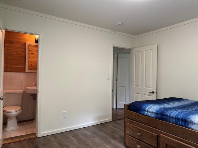 bedroom featuring dark tile patterned floors, connected bathroom, sink, and tile walls