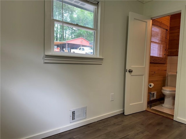 unfurnished bedroom featuring ensuite bathroom, wooden walls, and dark hardwood / wood-style flooring