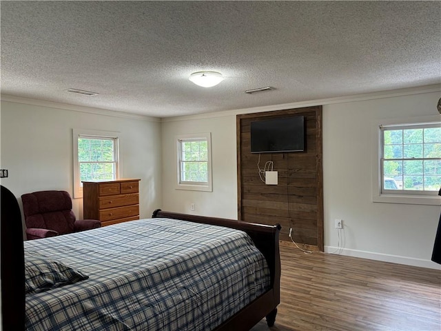 bedroom with a textured ceiling, wood-type flooring, and ornamental molding