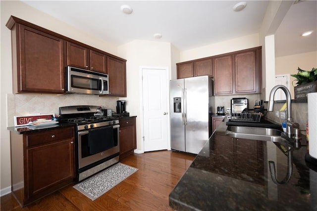 kitchen with backsplash, stainless steel appliances, dark wood-type flooring, sink, and dark stone countertops