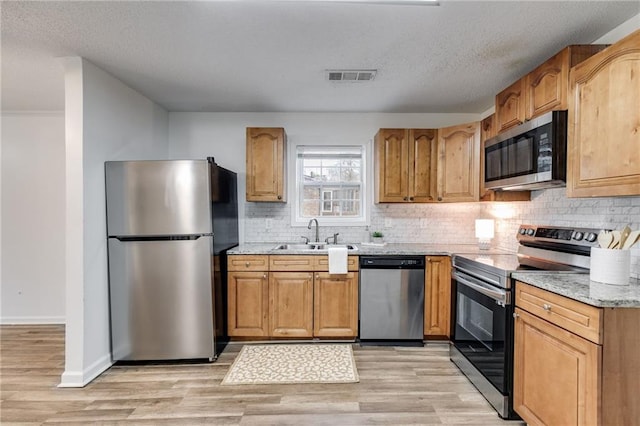 kitchen with sink, light stone counters, appliances with stainless steel finishes, light hardwood / wood-style floors, and backsplash