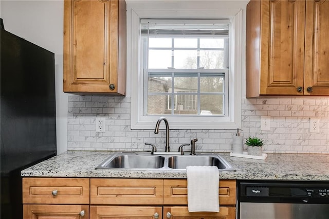 kitchen with sink, light stone counters, black refrigerator, stainless steel dishwasher, and decorative backsplash