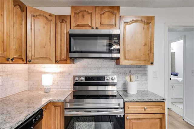 kitchen with stainless steel appliances, light stone countertops, backsplash, and light hardwood / wood-style floors