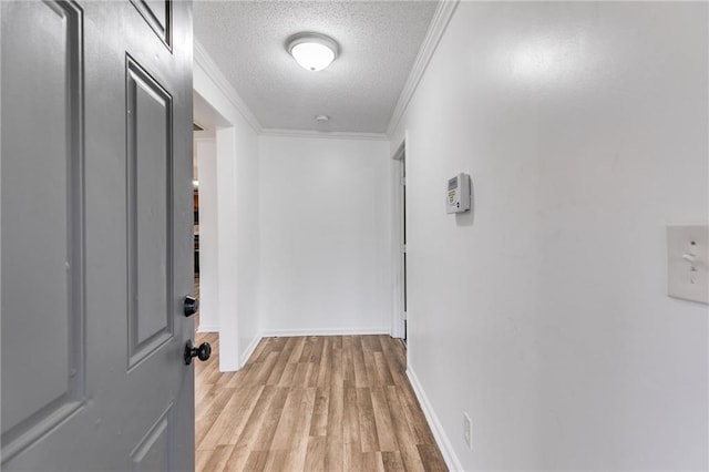 hallway with ornamental molding, light wood-type flooring, and a textured ceiling