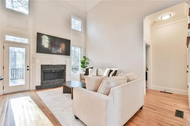 living room with a stone fireplace, light hardwood / wood-style flooring, a wealth of natural light, and a high ceiling