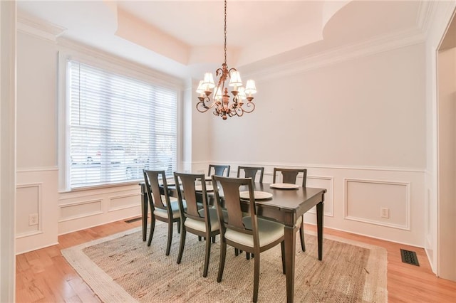 dining area with an inviting chandelier, a tray ceiling, light hardwood / wood-style floors, and crown molding