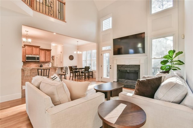 living room featuring a high ceiling, a notable chandelier, light wood-type flooring, and a fireplace