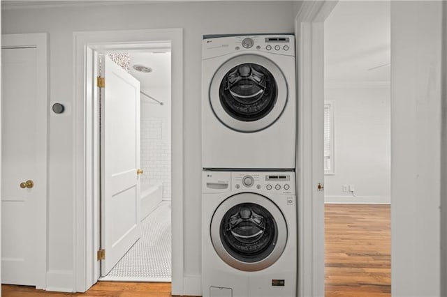 laundry room with wood-type flooring, crown molding, and stacked washer / dryer