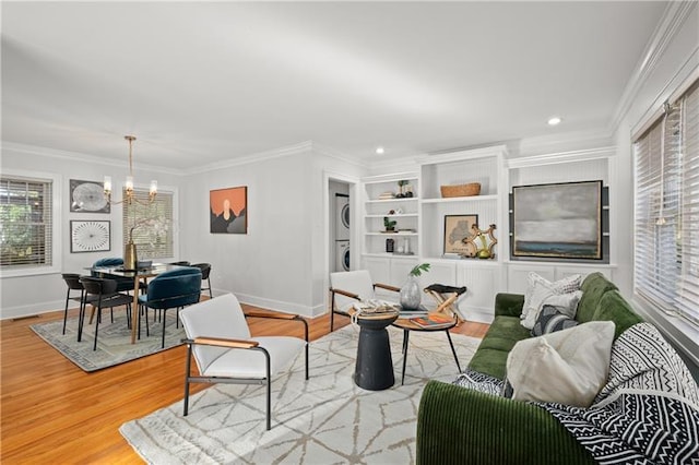 living room featuring stacked washer / drying machine, wood-type flooring, a chandelier, and ornamental molding