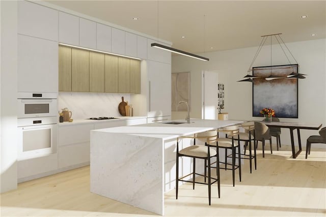 kitchen with light hardwood / wood-style floors, a kitchen island with sink, sink, white cabinetry, and double oven