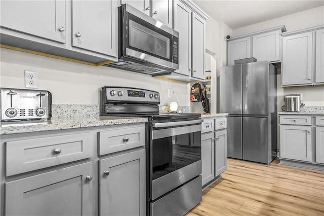 kitchen with appliances with stainless steel finishes, light wood-style floors, gray cabinetry, and light stone countertops