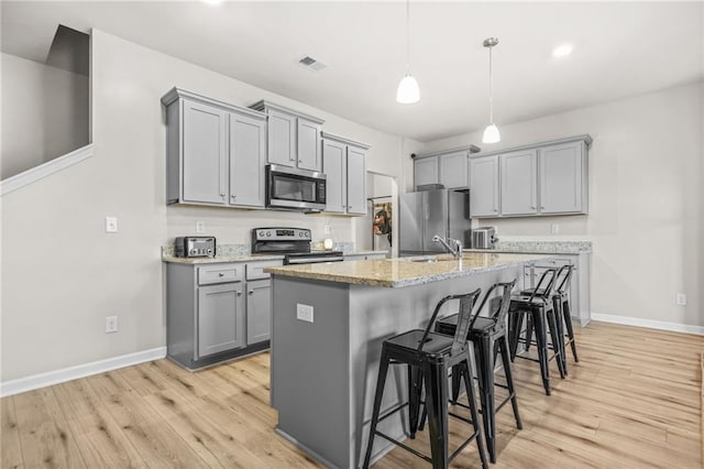 kitchen with a kitchen breakfast bar, visible vents, light wood-style floors, gray cabinetry, and appliances with stainless steel finishes