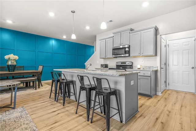 kitchen with light wood finished floors, gray cabinets, appliances with stainless steel finishes, and a kitchen island with sink