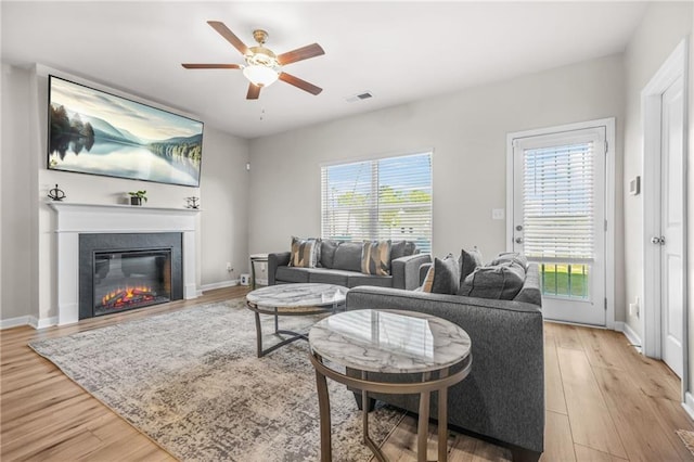 living room featuring light wood-style floors, ceiling fan, a glass covered fireplace, baseboards, and visible vents