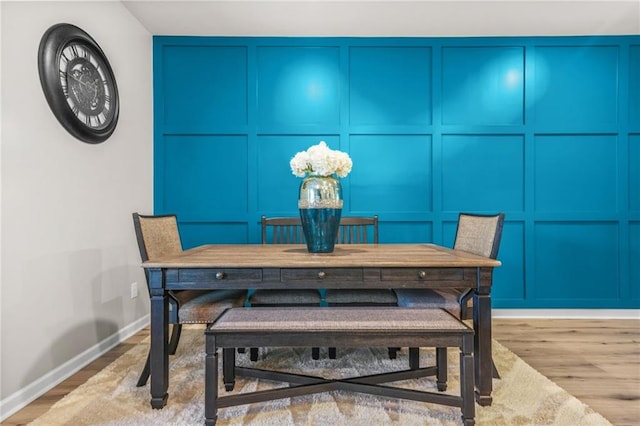 dining room with wood finished floors, a decorative wall, and baseboards