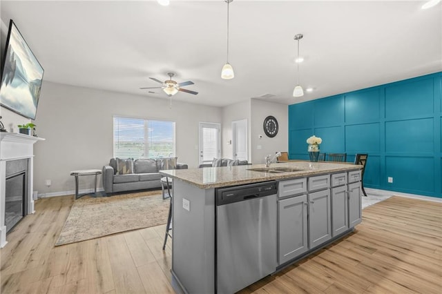 kitchen featuring a sink, light wood-style floors, a ceiling fan, dishwasher, and an island with sink
