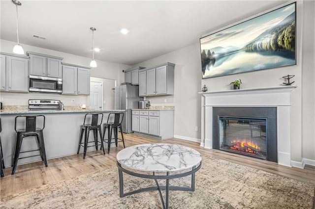 living room with baseboards, a glass covered fireplace, light wood-style floors, and visible vents