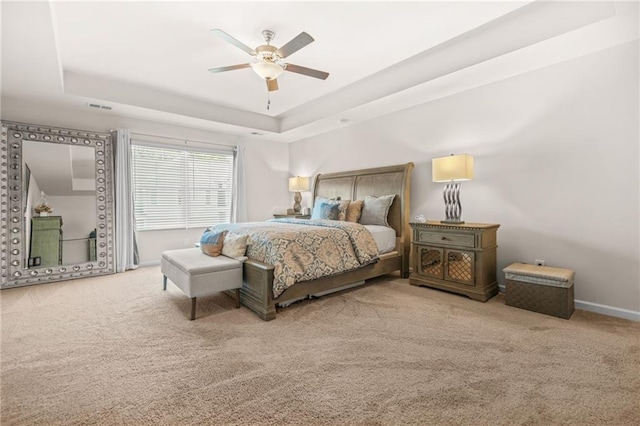 carpeted bedroom with a tray ceiling, visible vents, a ceiling fan, and baseboards